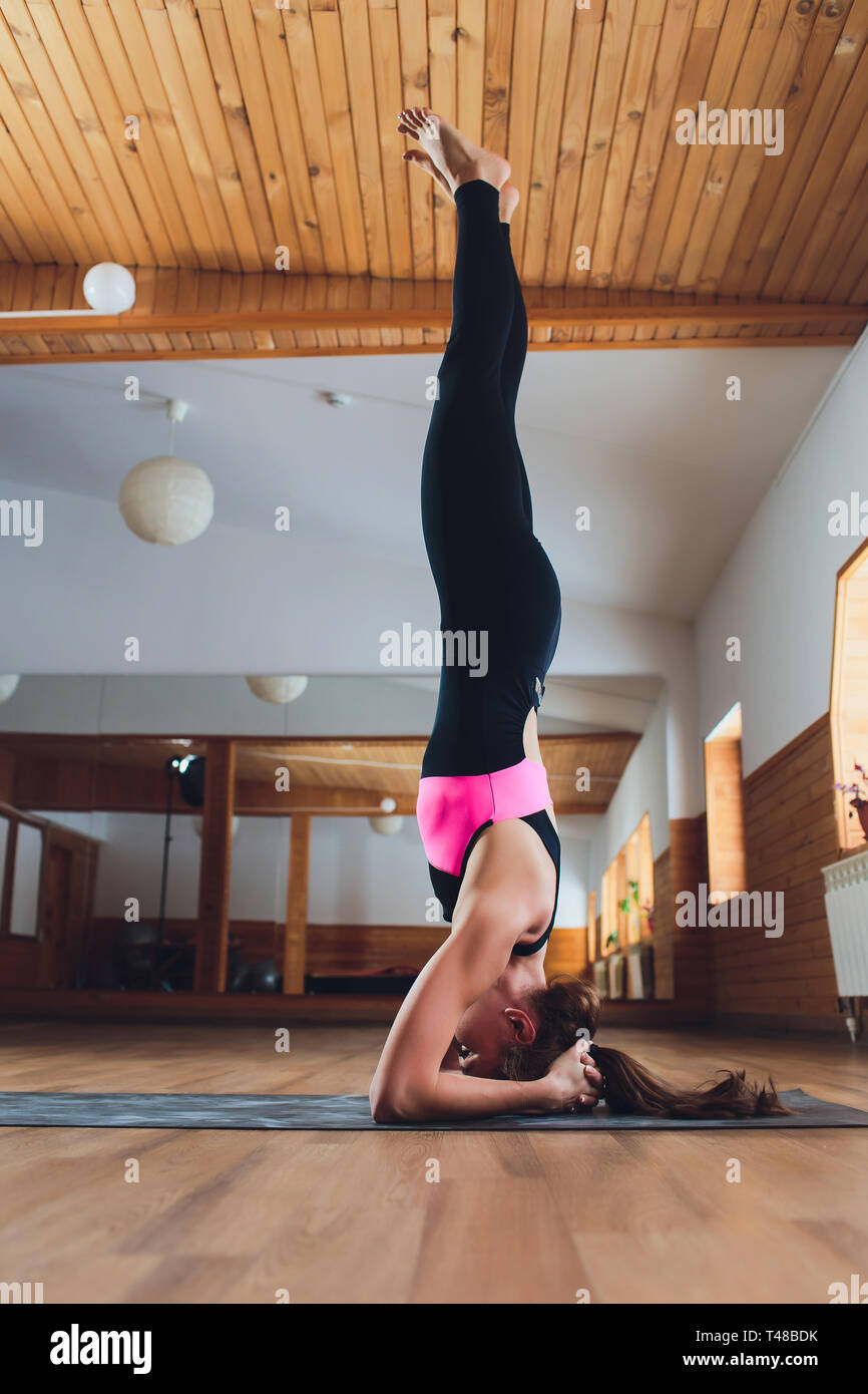 Junge Yogi attraktive Frau yoga Konzept, in salamba sirsasana Übung stehend, Kopfstand darstellen, Arbeiten, Sportkleidung tragen, schwarz Stockfoto