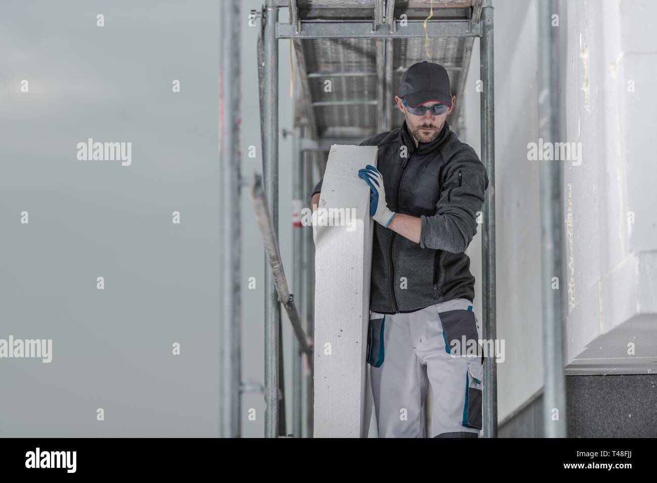 Kaukasische Auftragnehmer Arbeiter mit Stück Isolierung Gehen auf einem Gerüst. Stockfoto