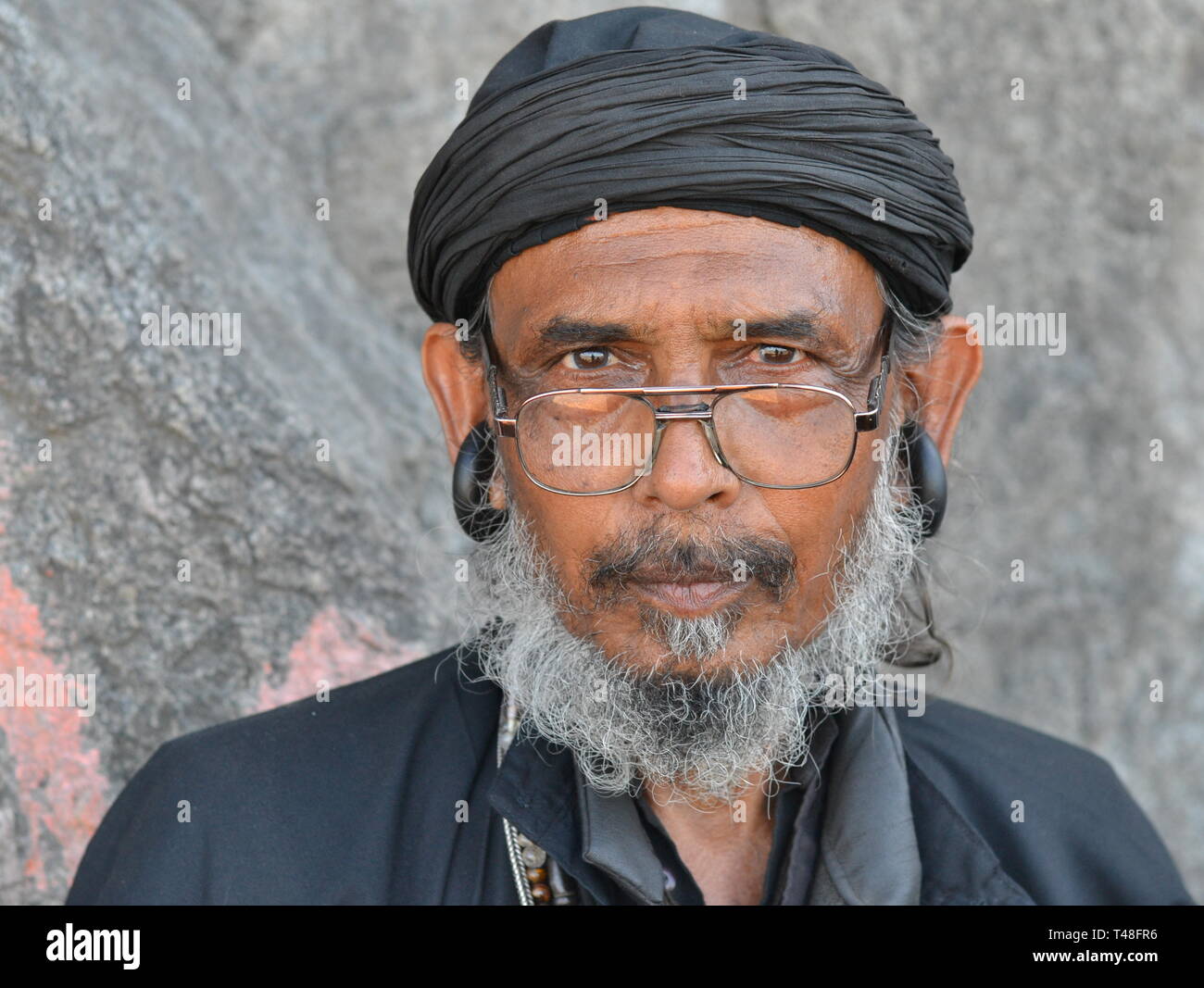 Indische Gorakhnathi (Kanphata) Yogi/Mönch, gekleidet in schwarz, trägt markante Grosse des Gorakh-Nath um Ohrringe und Einblicke über seine Brille. Stockfoto