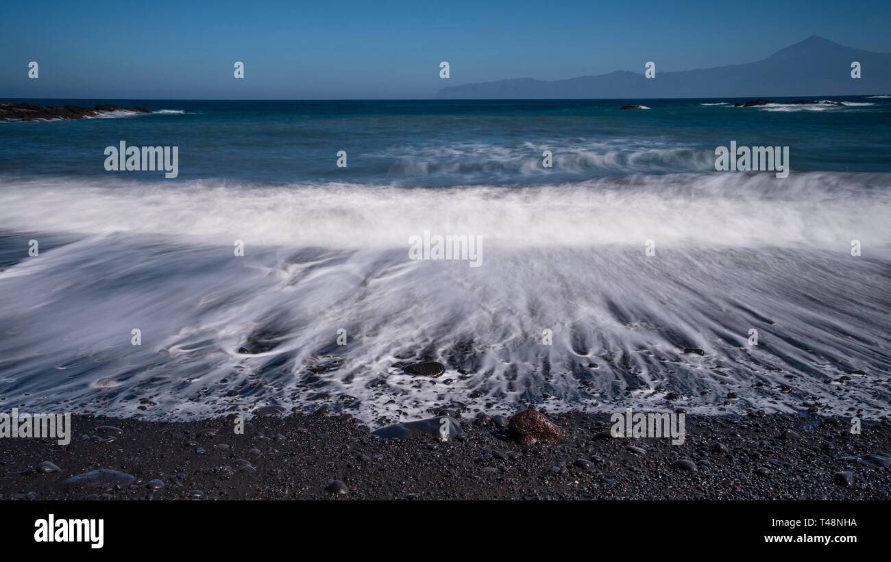 Schwarze Kieselstrand mit Wave Saum, Langzeitbelichtung, Blick zum Teide auf Teneriffa, Puerto de La Caleta, La Gomera, Kanarische Inseln, Spanien Stockfoto