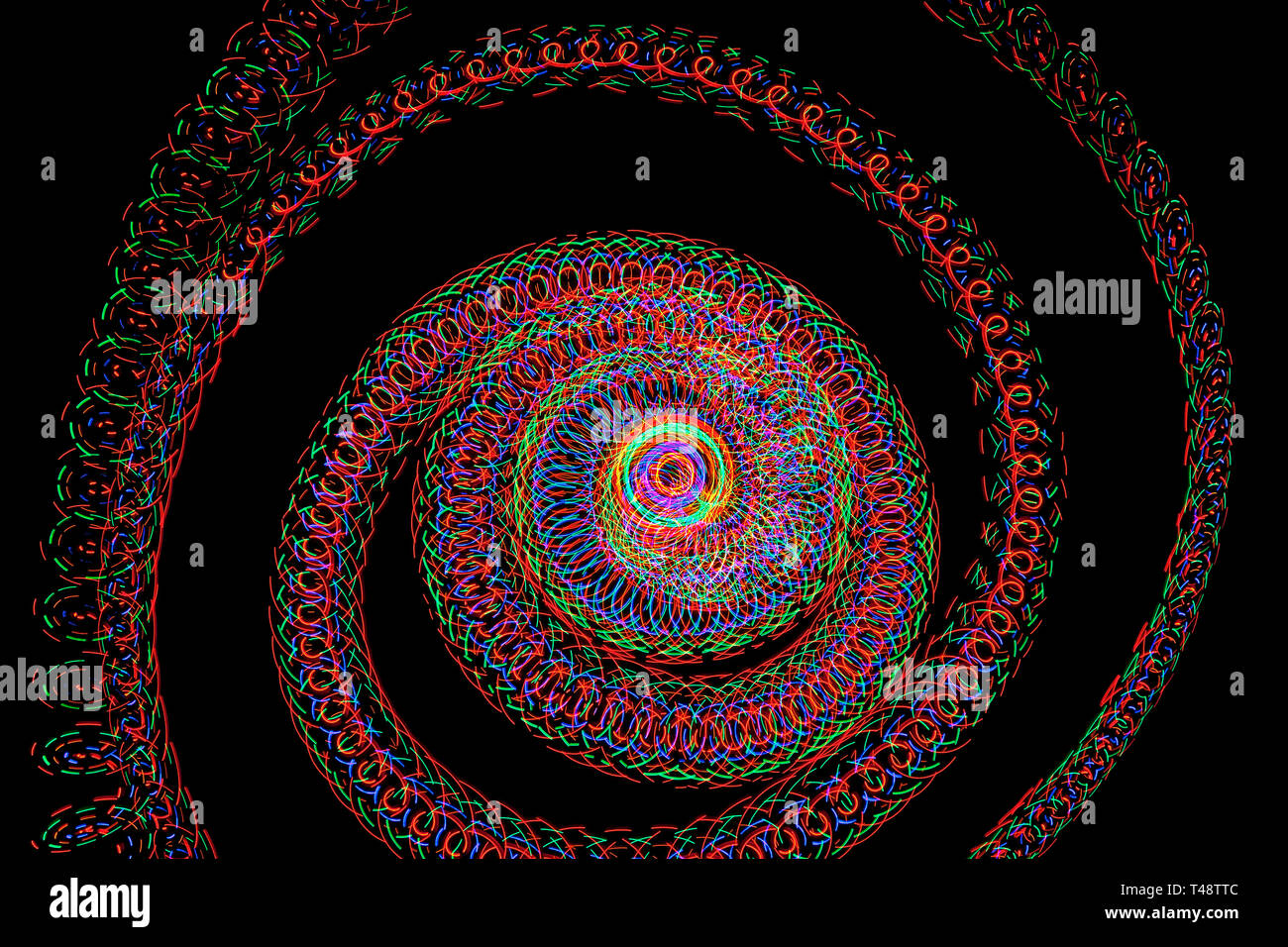 Mehrfarbige spiralförmige Lichtspuren blühen auf einem tiefschwarzen Hintergrund und bilden komplizierte hypnotische Muster, die mit Bewegung und lebendiger Energie pulsieren. Stockfoto