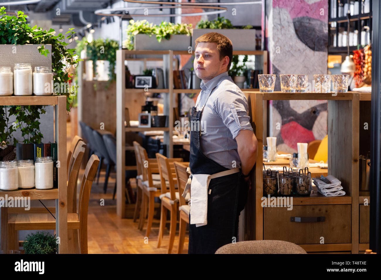 Russland Novosibirsk 2018-11-26 Eine junge männliche Kellner in Uniform, Hemd und schwarze Schürze steht im Restaurant und beobachten die Verkaufsfläche und Kund. Stockfoto