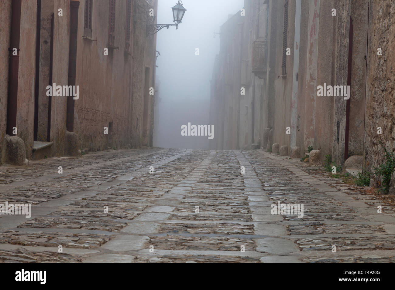 Gepflasterte Straße in einer mittelalterlichen Altstadt an einem nebligen Morgen, Erice, Sizilien, Italien. Stockfoto