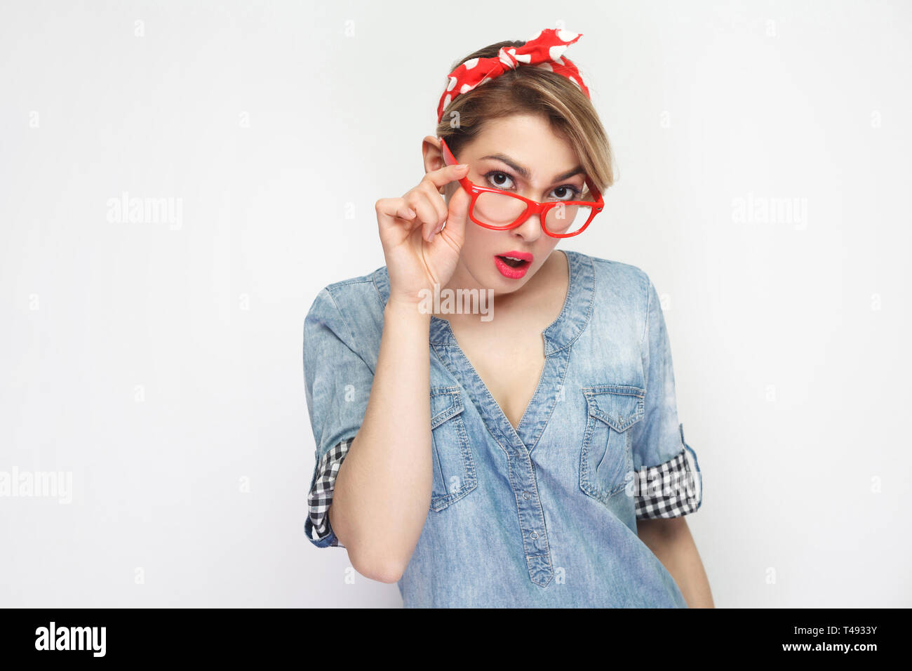 Portrait von aufmerksamen schöne junge Frau in lässigem Blue Denim Shirt mit Make-up und roten Stirnband ständigen Holding Brille und Kamera. Stockfoto