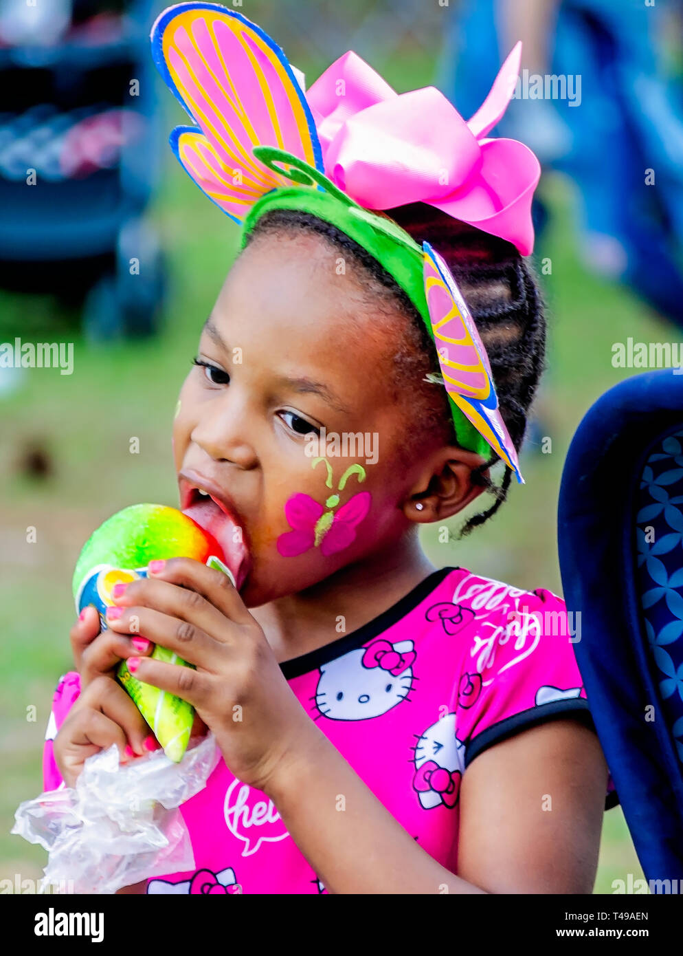 Ein Mädchen im bunny Ohren frisst einem regenbogenfarbenen Sno-Kegel während einer Gemeinschaft Ostereiersuche am Langan Park, April 13, 2019 in Mobile, Alabama. Stockfoto