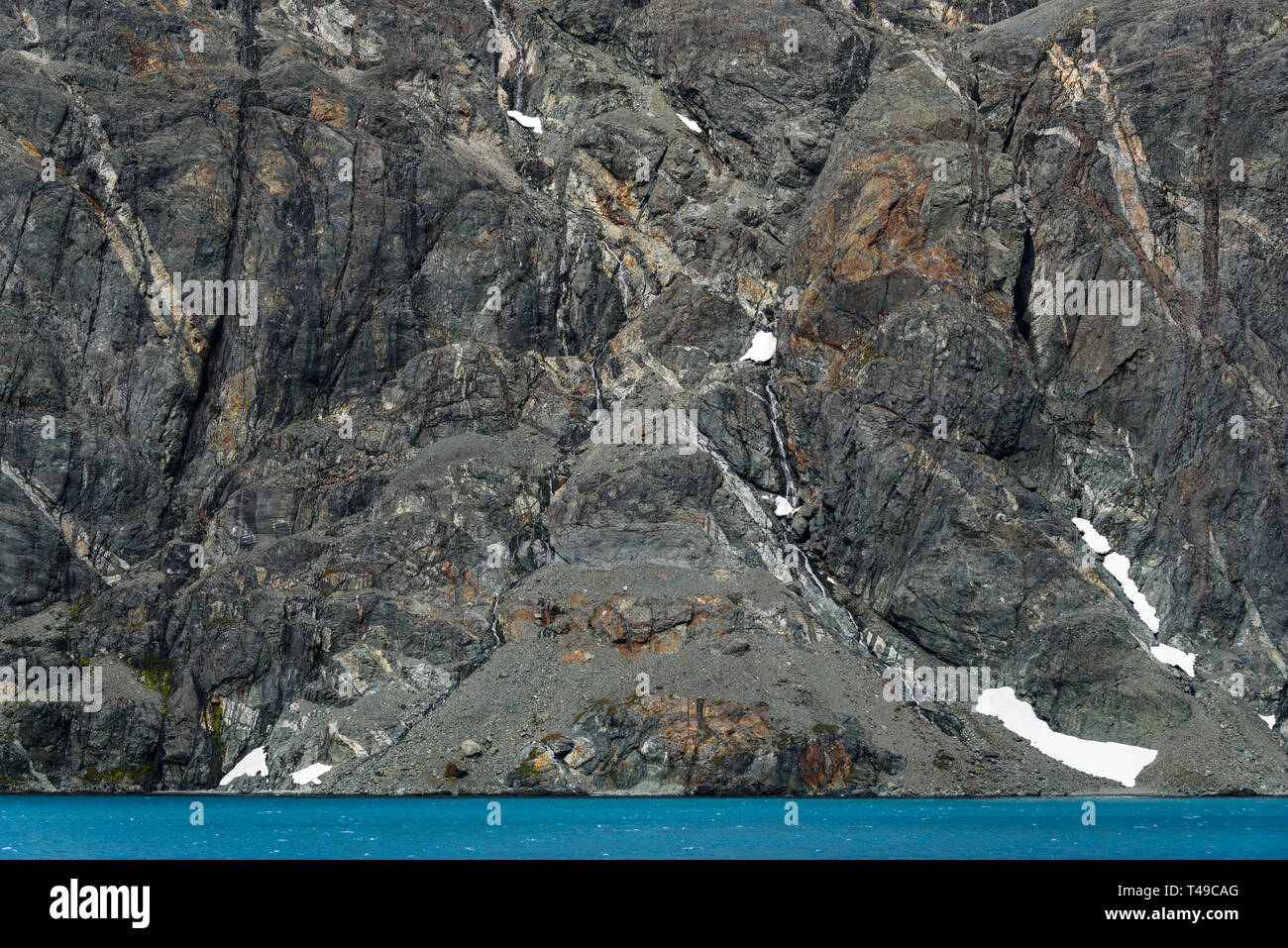 Verwitterten grauen Felswand mit Orange und Weiß mineral Venen, Schnee, Patches, und glazialen blaues Wasser, Drygalski Fjord, Südgeorgien Stockfoto