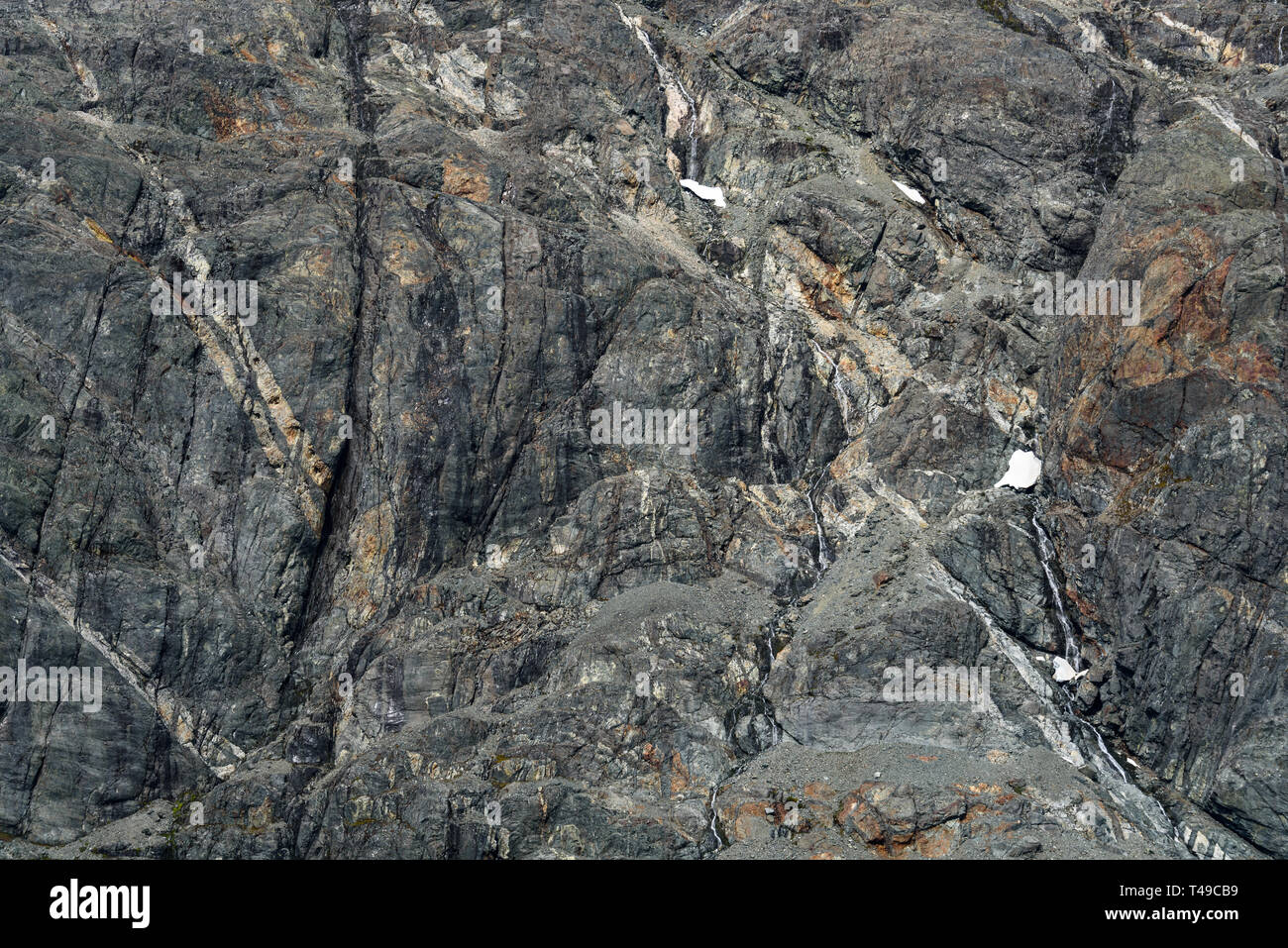 Verwitterten grauen Felswand mit Orange und Weiß mineral Venen als Natur Hintergrund Stockfoto