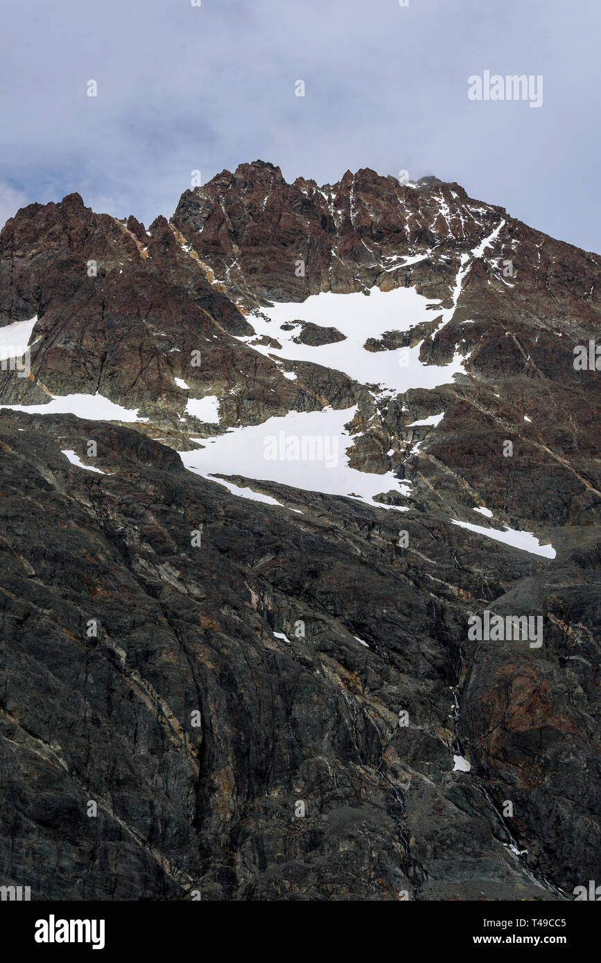 Schönen felsigen Bergspitzen mit Adern orange Mineralien, Schnee, Patches und blauer Himmel mit weißen Wolken wispy Stockfoto