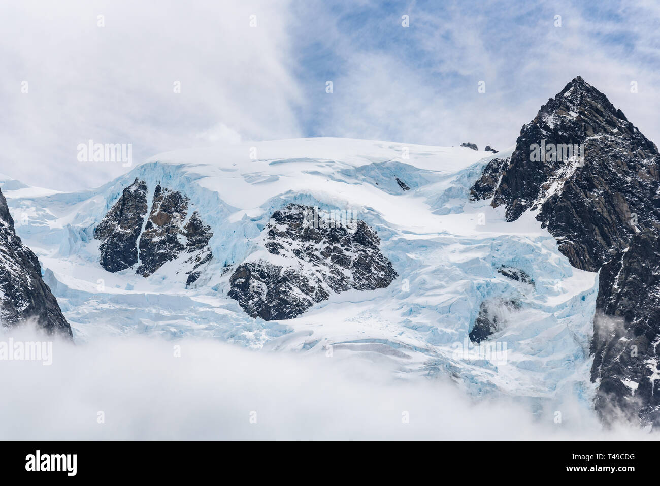 Schnee und Gletscher Eis bedeckt Rocky Mountain Peak, mit Nebel unten und leichte weiße Wolken am blauen Himmel, die Drygalski Fjord, Südgeorgien Stockfoto