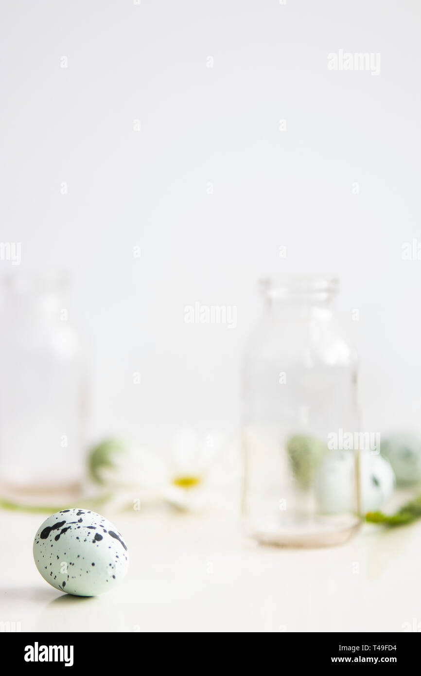 Gesprenkelte robin Ei auf weiße Oberfläche mit unscharf Glaswaren und Blumen im Hintergrund. High-key. Kopieren Sie Platz. Stockfoto