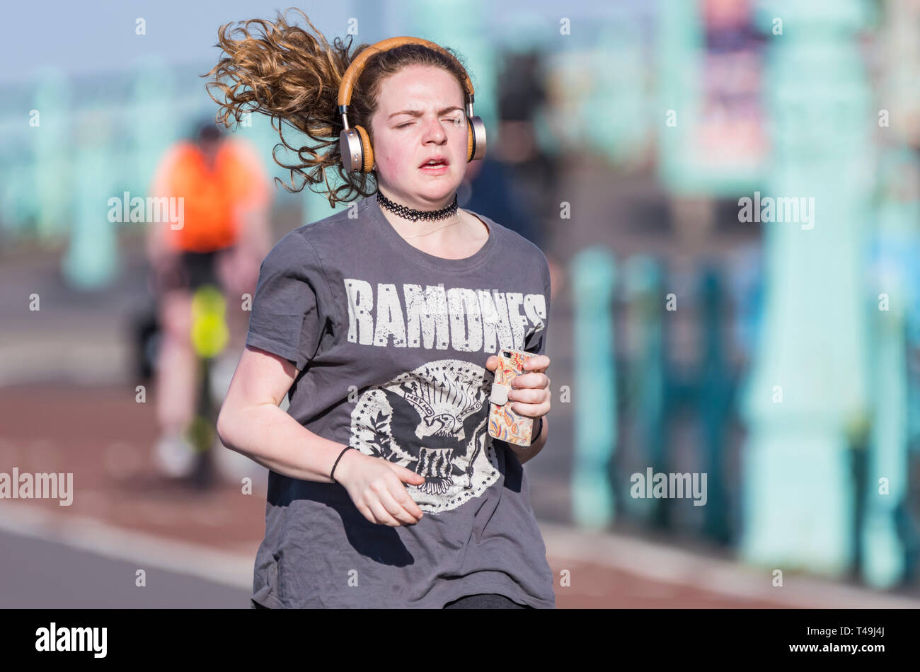 Vorderansicht einer jungen Frau joggen mit Haare fliegen in den Wind, das Tragen von Kopfhörern, die im Frühjahr in Großbritannien. Gesunde Lebensweise. Stockfoto