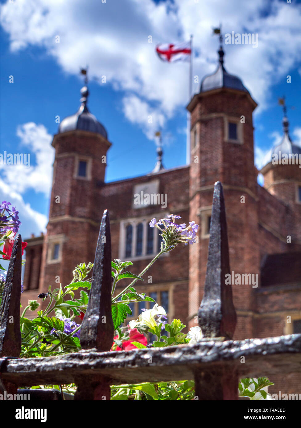 Das historische Guildford Großbritannien Frühling Blumen durch alte Geländer im Vordergrund und Kreuz von St. George flag gesehen auf Jacobean Abbot's Krankenhaus in Surrey UK Stockfoto