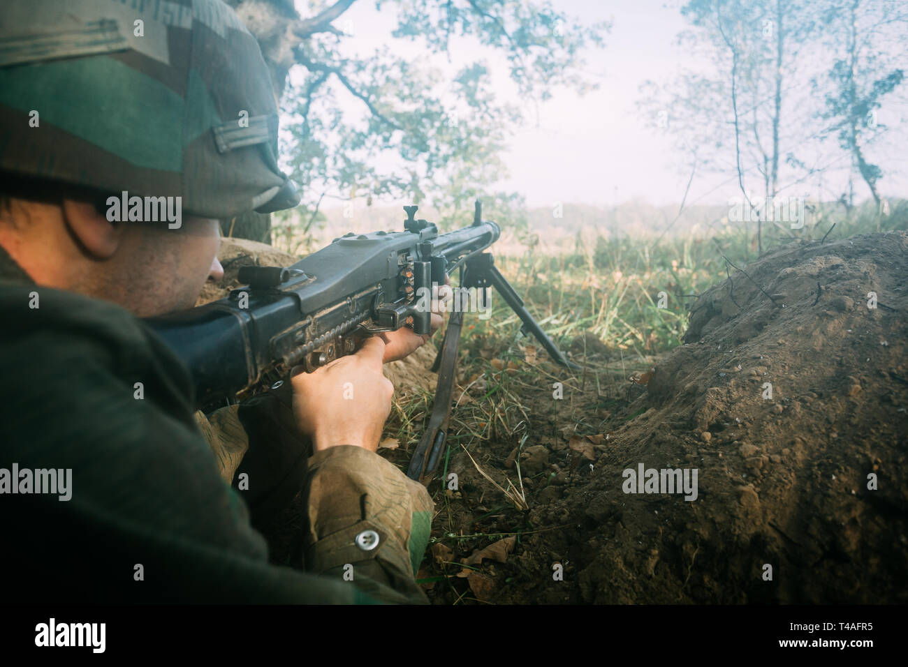 Versteckte Re-Enactor als Deutsche Wehrmacht Infanterie Soldat im Zweiten Weltkrieg mit dem Ziel, ein Maschinengewehr auf gegnerische aus Graben In nebligen Wald gekleidet. WWII WW2 Wea Stockfoto