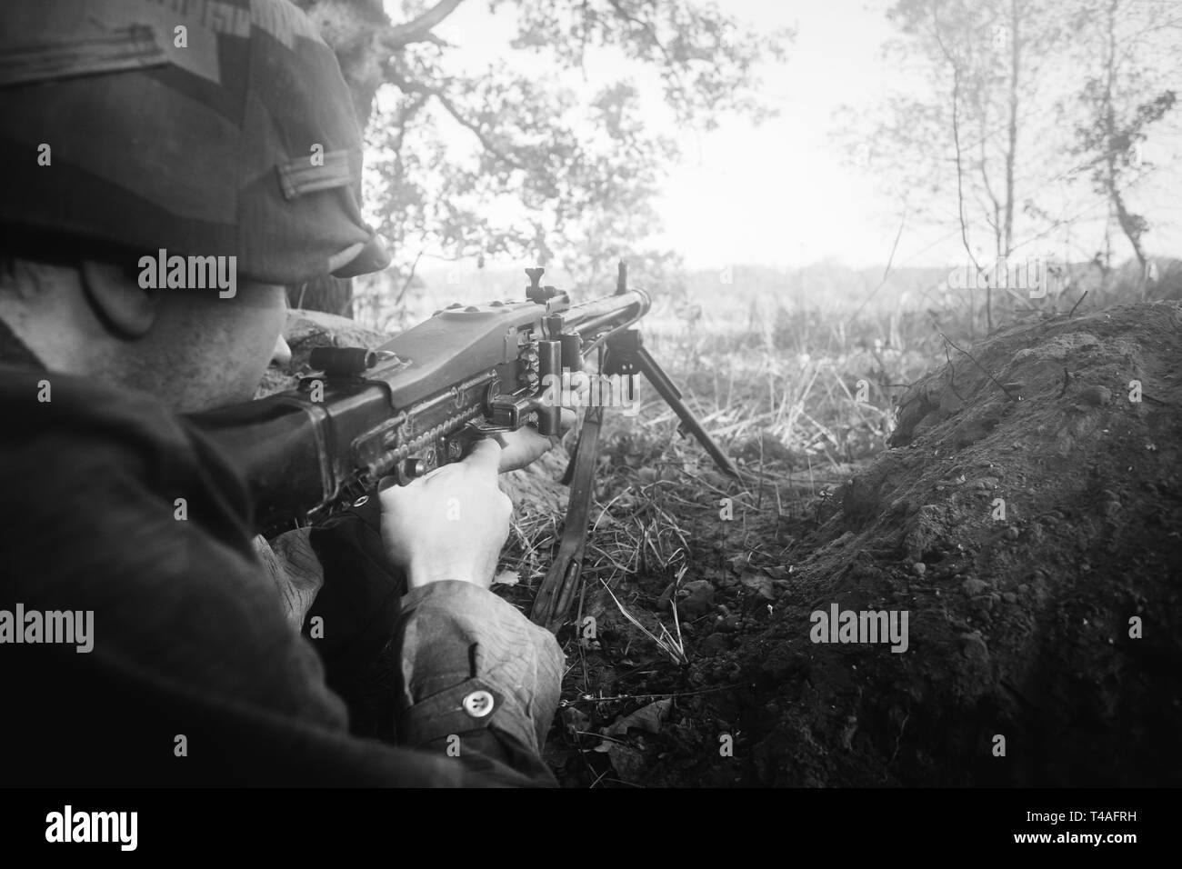 Versteckte Re-Enactor als Deutsche Wehrmacht Infanterie Soldat im Zweiten Weltkrieg mit dem Ziel, ein Maschinengewehr aus dem Graben In nebligen Wald gekleidet. WWII WW2 Waffe MG42 Stockfoto