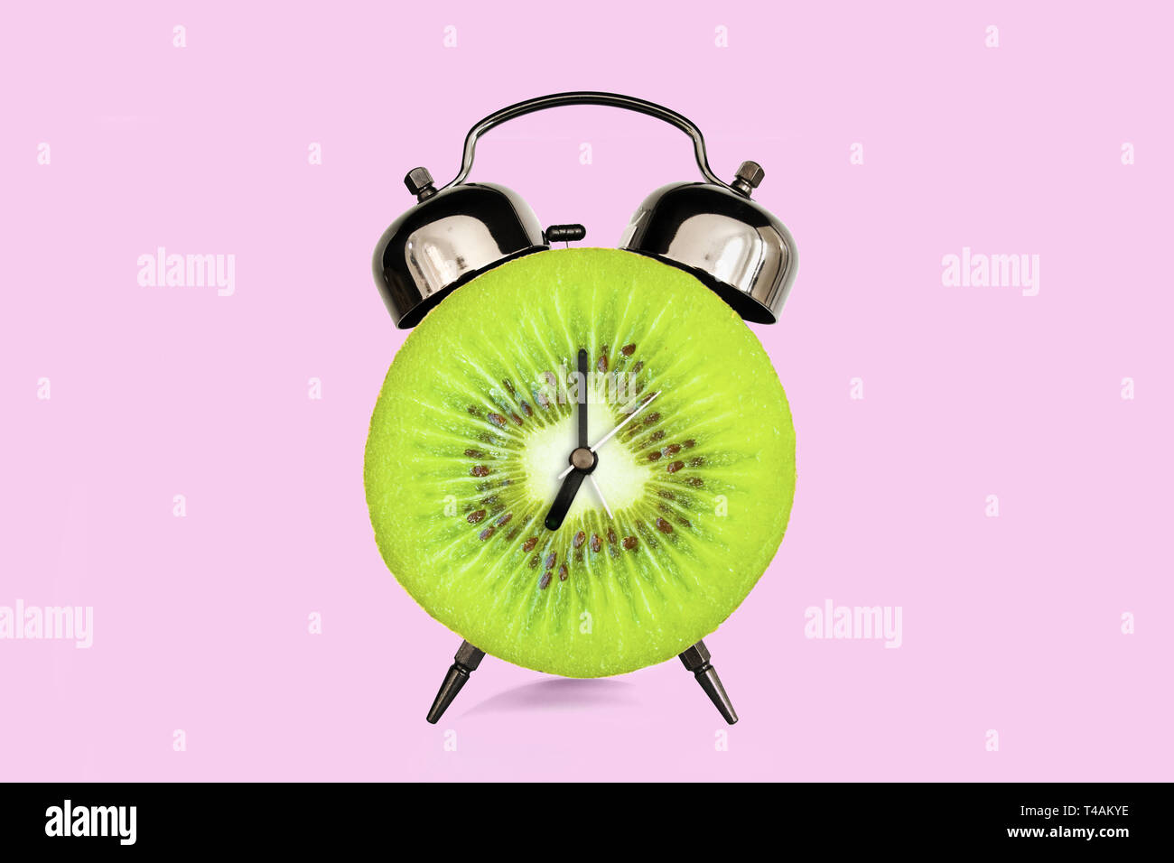 Kiwi Slice auf Wecker, Rosa pastell Hintergrund. Obst und Vitamine Ernährung beim Frühstück Ernährung Konzept Stockfoto