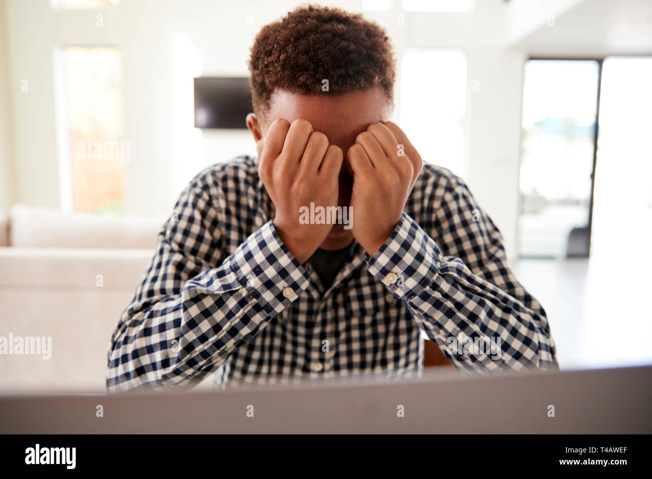 Schwarzen Teenager mit Kopf in den Händen mit einem Laptop Computer zu Hause, Vorderansicht, in der Nähe Stockfoto