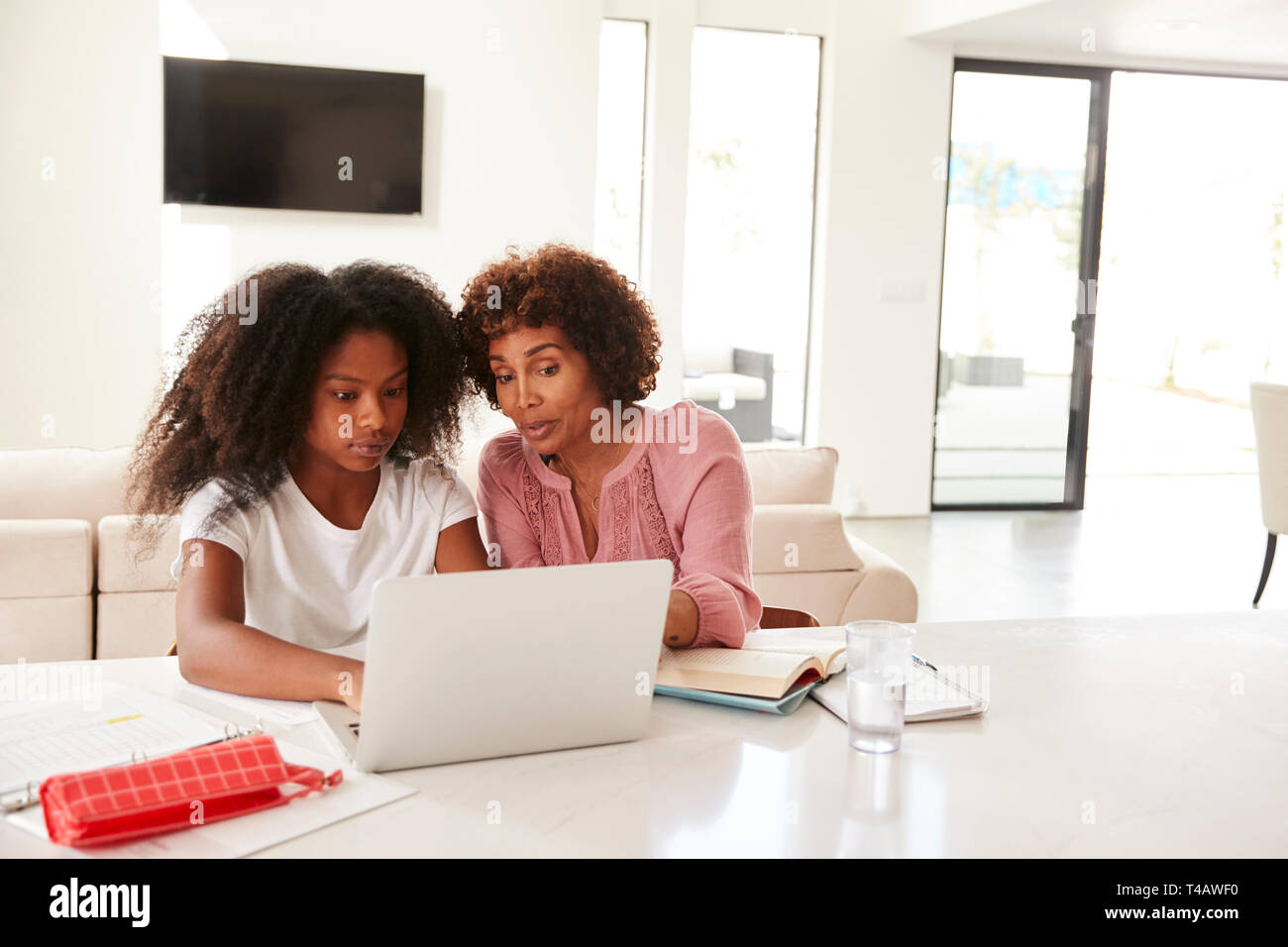 Im mittleren Alter schwarze Frau, die ihre Tochter im Teenageralter helfen bei Hausaufgaben, Vorderansicht Stockfoto