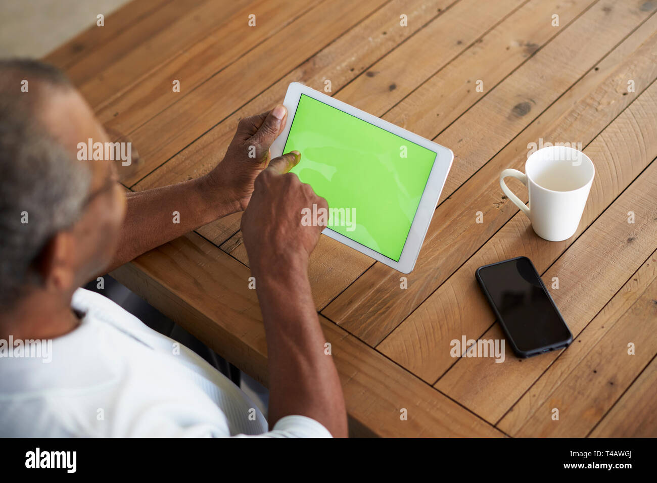 Älteren schwarzen Mann am Tisch sitzen mit Tablet-PC, Erhöhte Ansicht über die Schulter Stockfoto