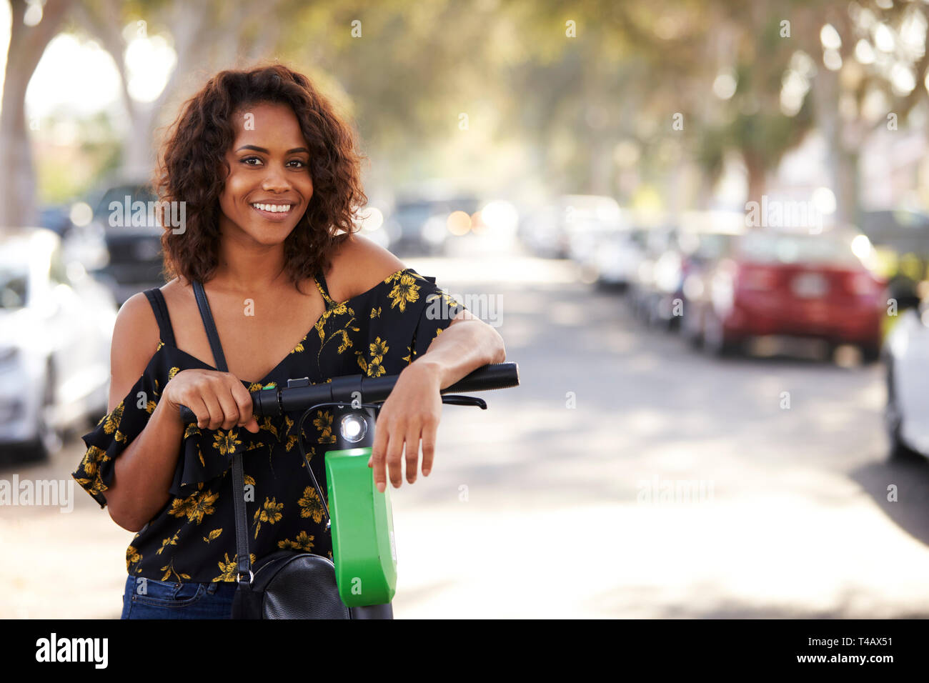 In der Nähe des Tausendjährigen schwarze Frau Schiefen auf einem elektrischen scooter auf der Straße, ein Lächeln für die Kamera Stockfoto