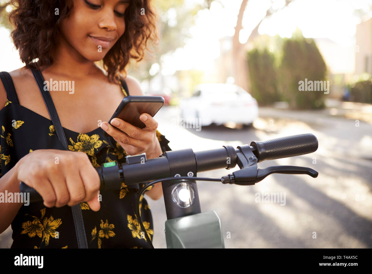 Tausendjährige schwarze Frau auf einem Elektroroller mit Smartphone, in der Nähe Stockfoto