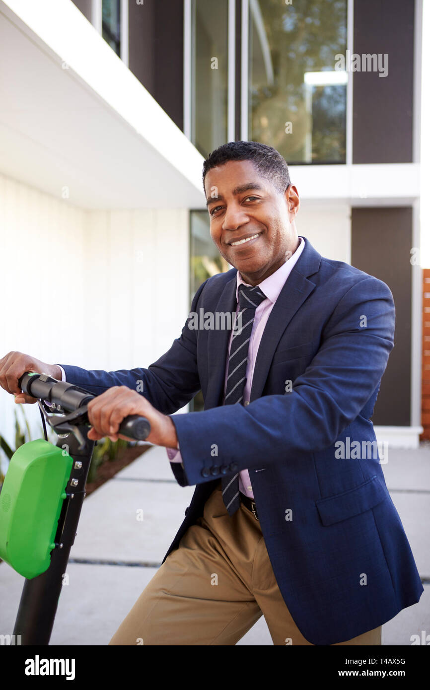 Intelligent im mittleren Alter schwarzer Mann stehend auf elektroroller vor seinem Haus gekleidet, in der Nähe Stockfoto
