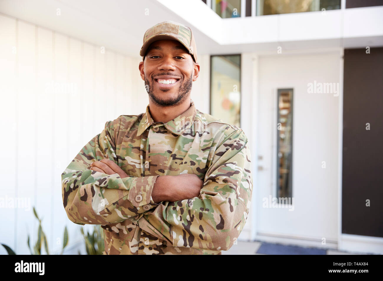 Soldat in der Tarnung außerhalb modernes Haus mit gekreuzten Armen lächelnd in die Kamera, in der Nähe Stockfoto