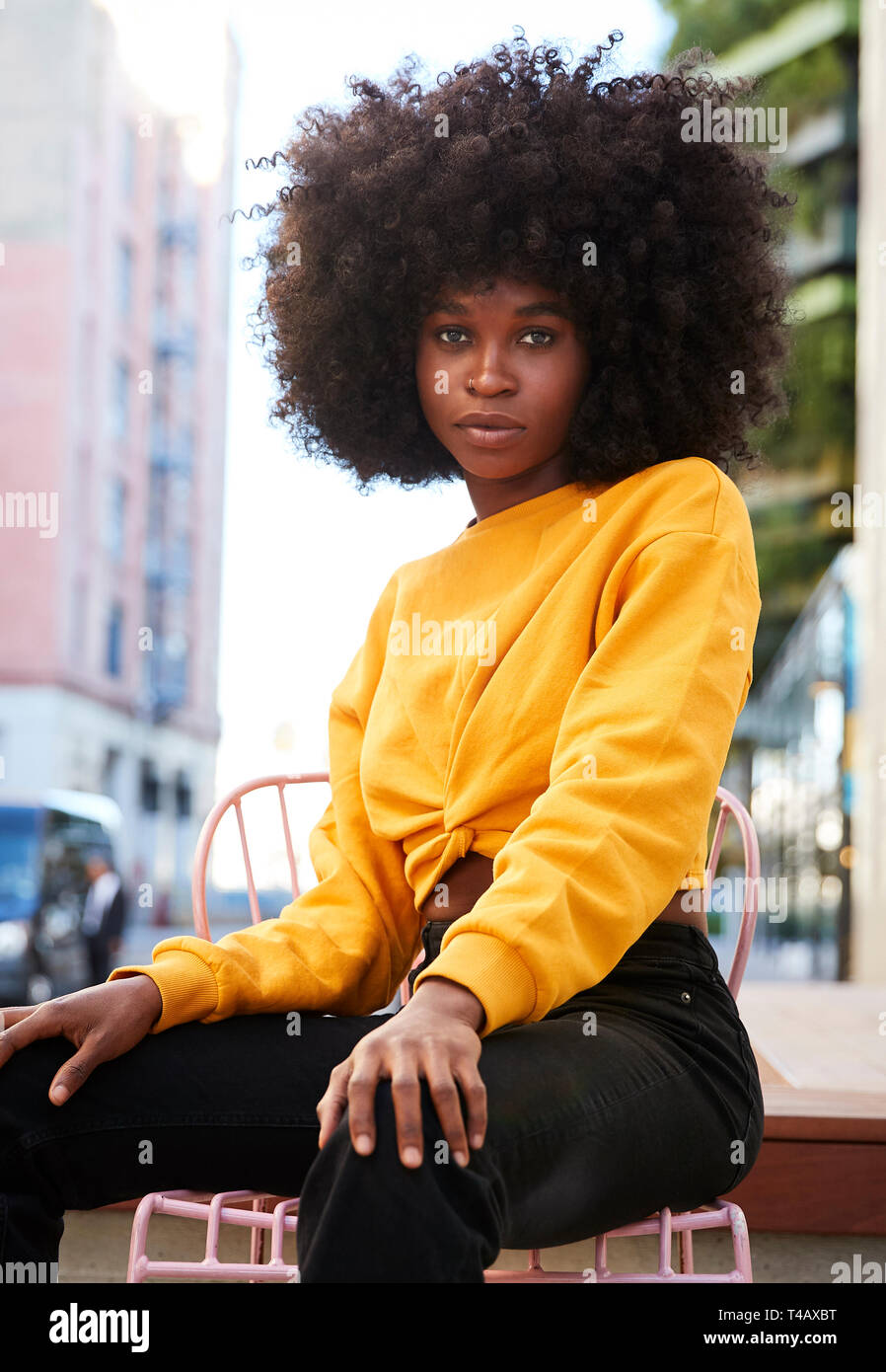Junge schwarze Frau mit afro Haar und sitzt auf einem Stuhl in der Straße an der Kamera, vertikal Stockfoto