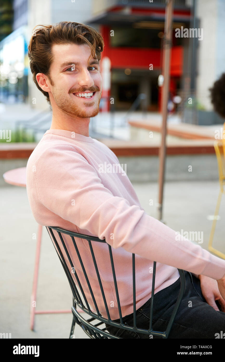 Tausendjährige weiß hipster Mann außerhalb ein Cafe in der Straße sitzen, dreht sich lächelnd in die Kamera, in der Nähe Stockfoto