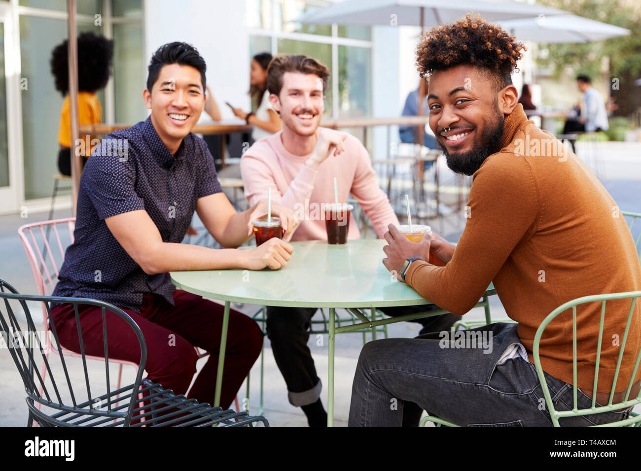 Drei tausendjährigen männliche Freunde reden über kalten Biere außerhalb ein Cafe in einer Stadt Straße biegen Sie auf die Kamera Stockfoto