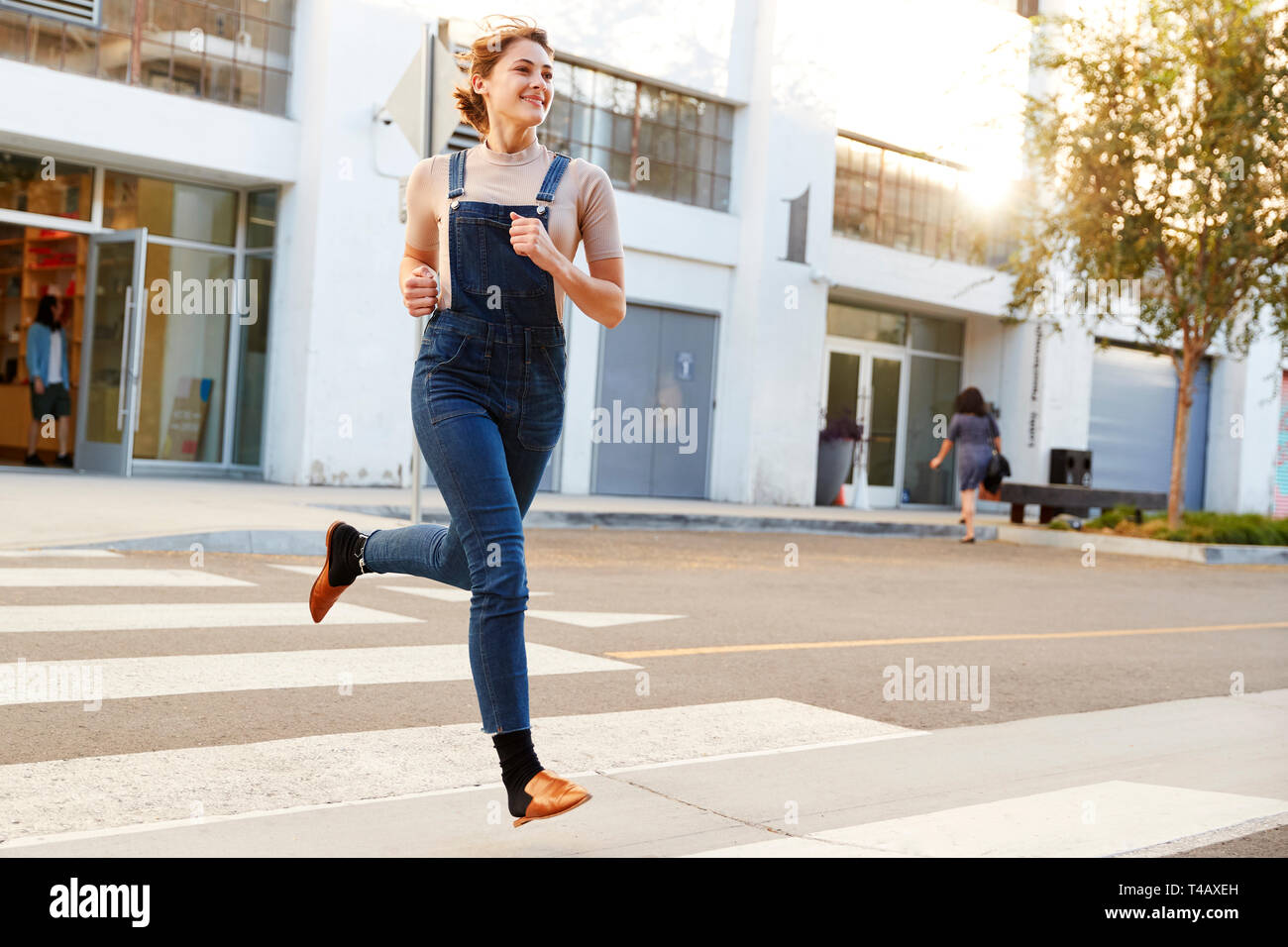 Modische junge Hispanic Frau in Latzhosen über die Straße laufen, volle Länge, Nahaufnahme Stockfoto