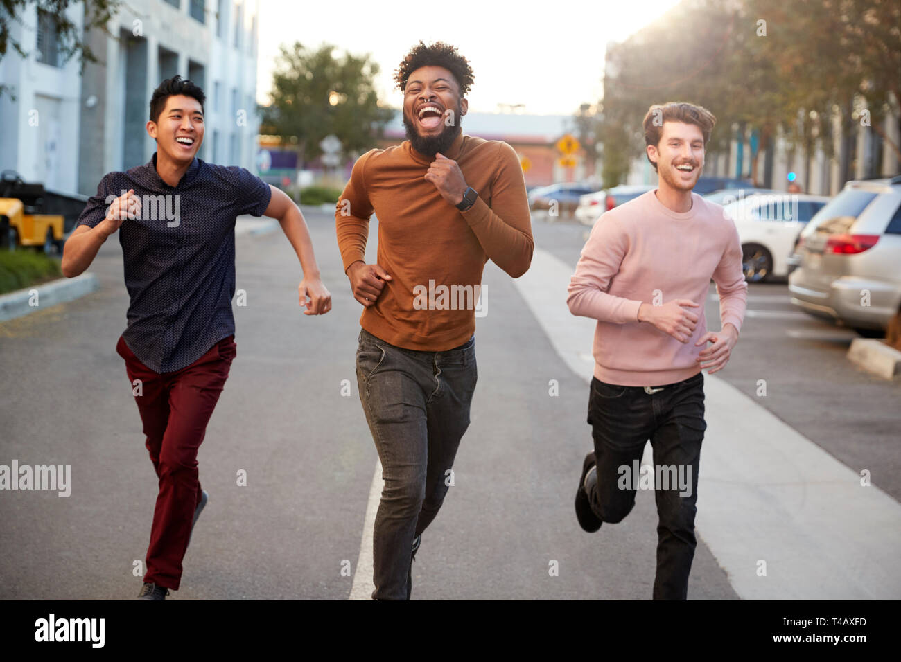 Drei hippen jungen erwachsenen männlichen Freunde laufen für Spaß in einer Stadt, Straße, Vorderansicht, drei Viertel Länge Stockfoto