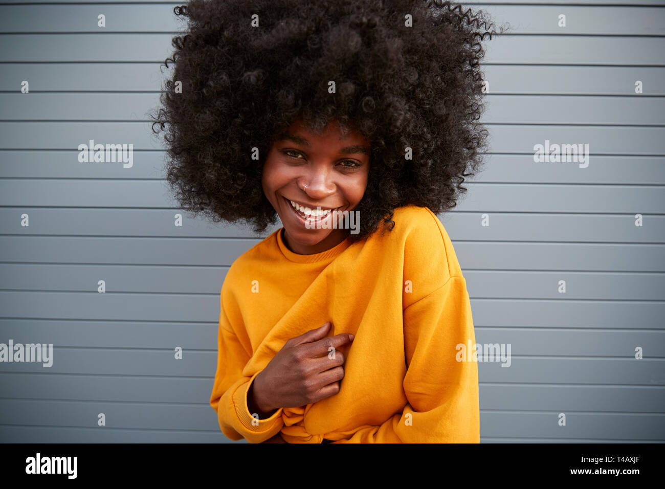 Junge schwarze Frau mit Afro gegen graue Wand, die Schulter und lächelt in die Kamera, in der Nähe Stockfoto