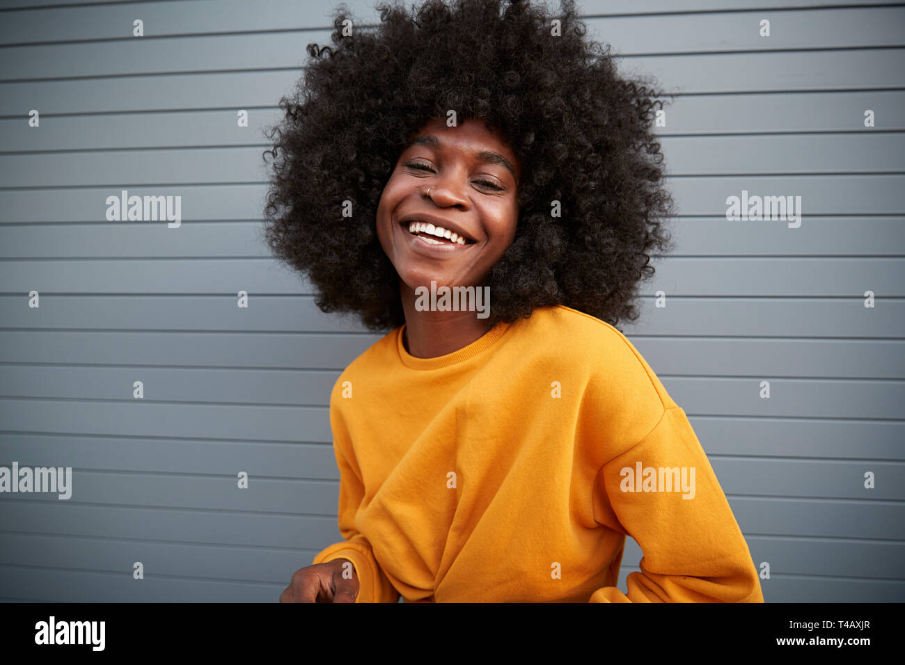 Junge schwarze Frau mit Afro stehend gegen Grau Sicherheit Rollläden, in die Kamera lachen, Nahaufnahme Stockfoto