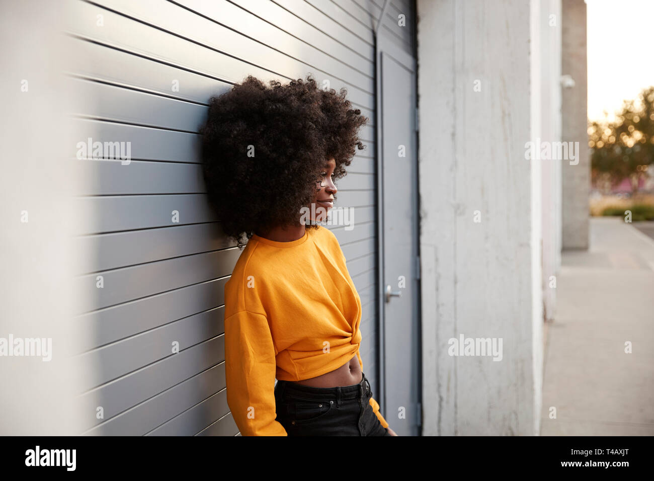 Junge schwarze Frau mit Afro in der Straße gegen Grau Sicherheit Rollläden schiefen, Seitenansicht Stockfoto