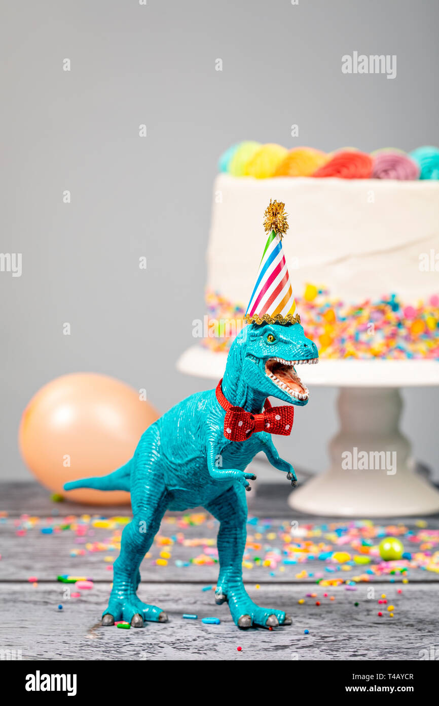 Spielzeug Dinosaurier bei einer Geburtstagsfeier mit Hut und Fliege. Stockfoto