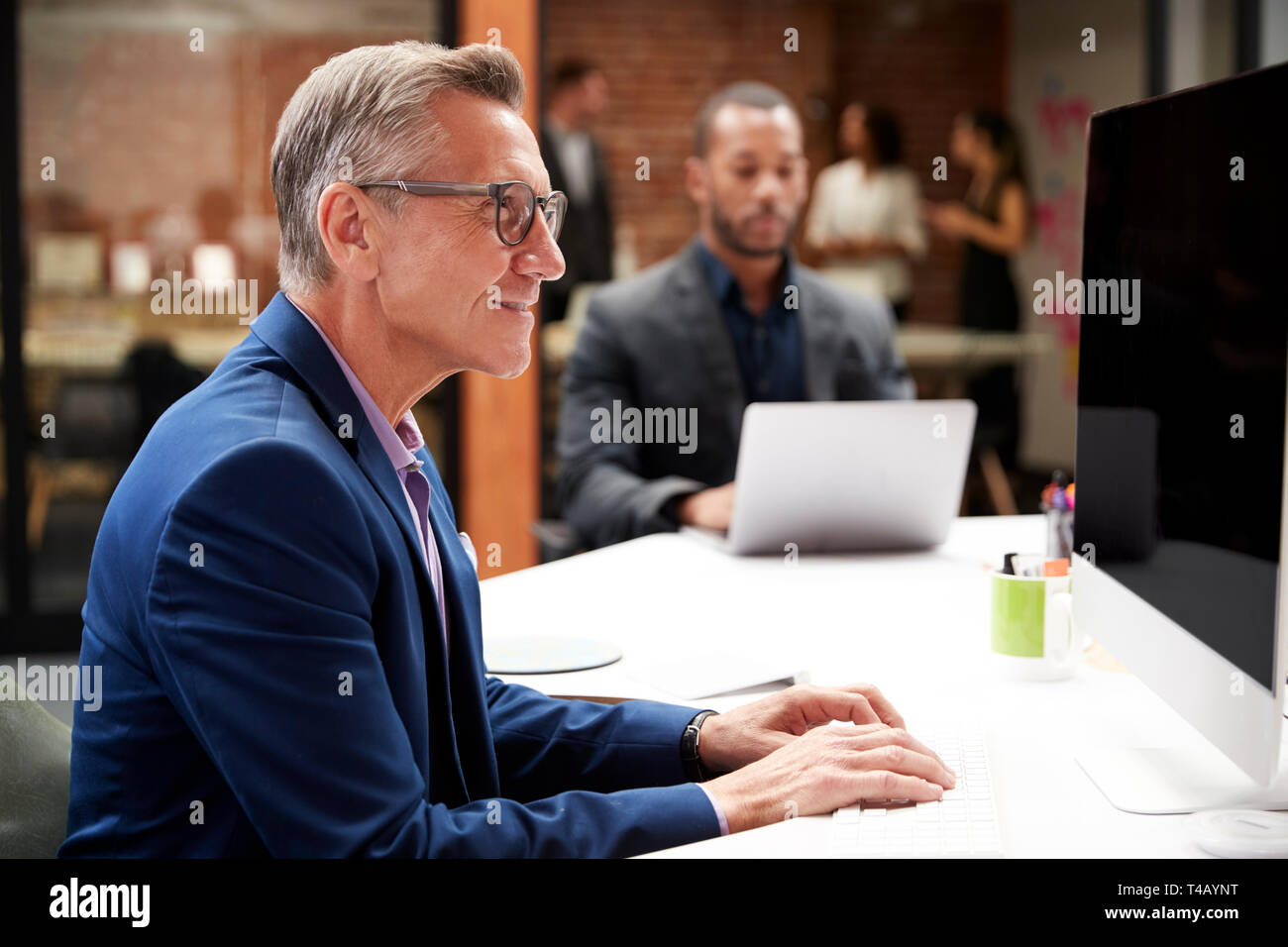 Reifen Geschäftsmanns, der am Schreibtisch auf dem Computer im Großraumbüro mit Kollegen im Hintergrund Stockfoto