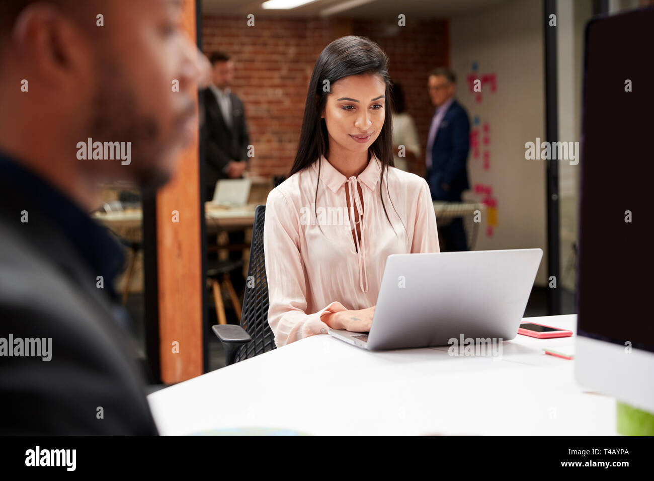 Geschäftsfrau am Laptop Arbeiten am Schreibtisch im Großraumbüro mit Kollegen im Hintergrund Stockfoto