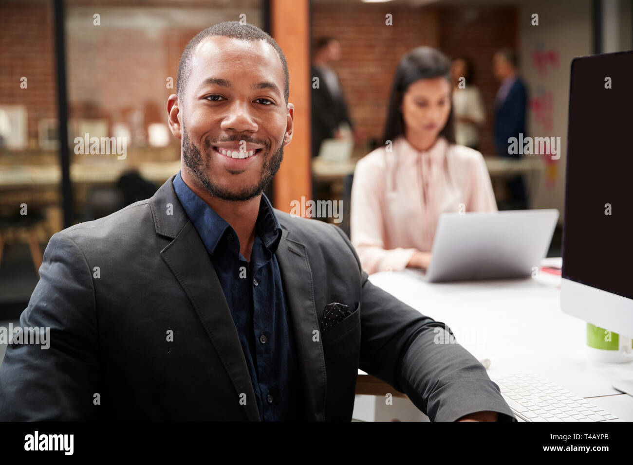 Porträt des Geschäftsmanns, der am Schreibtisch auf dem Computer im Großraumbüro mit Kollegen im Hintergrund Stockfoto