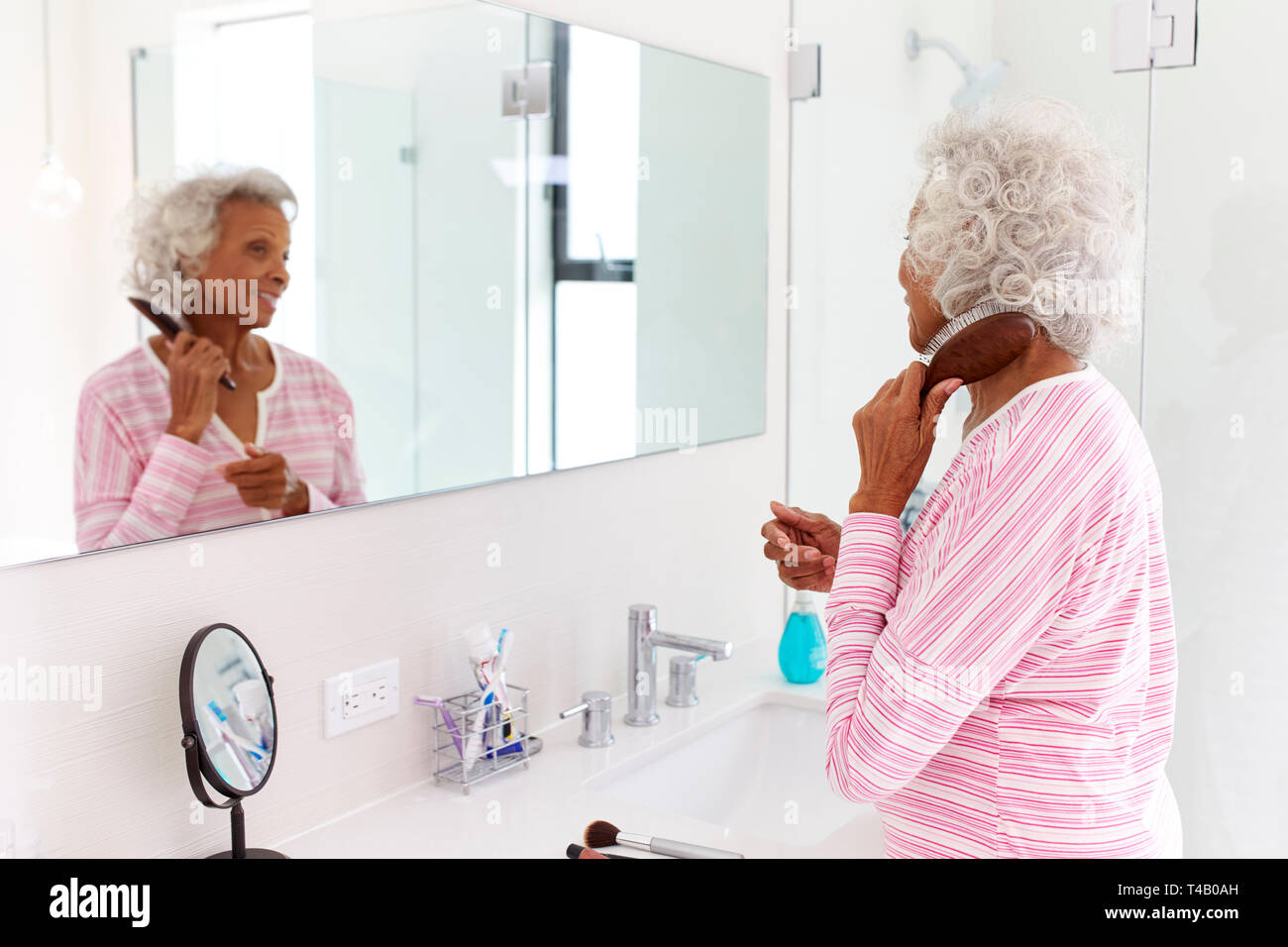 Ältere Frau auf der Suche nach Reflexion in Bad Spiegel putzen Haar Stockfoto