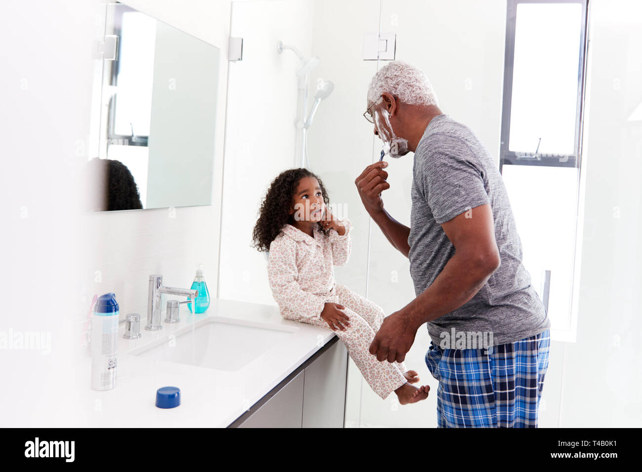 Großvater tragen Schlafanzug im Badezimmer rasieren Während Enkelin Uhren Stockfoto