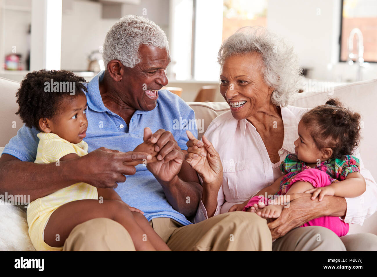 Großeltern Sitzen auf einem Sofa zu Hause spielt mit Baby Enkelinnen Stockfoto