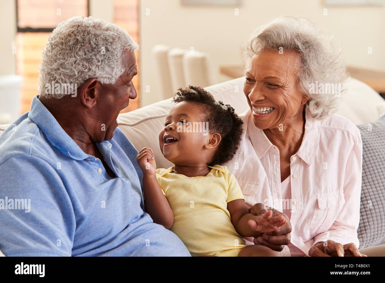 Großeltern Sitzen auf einem Sofa zu Hause spielt mit Baby Enkelin Stockfoto