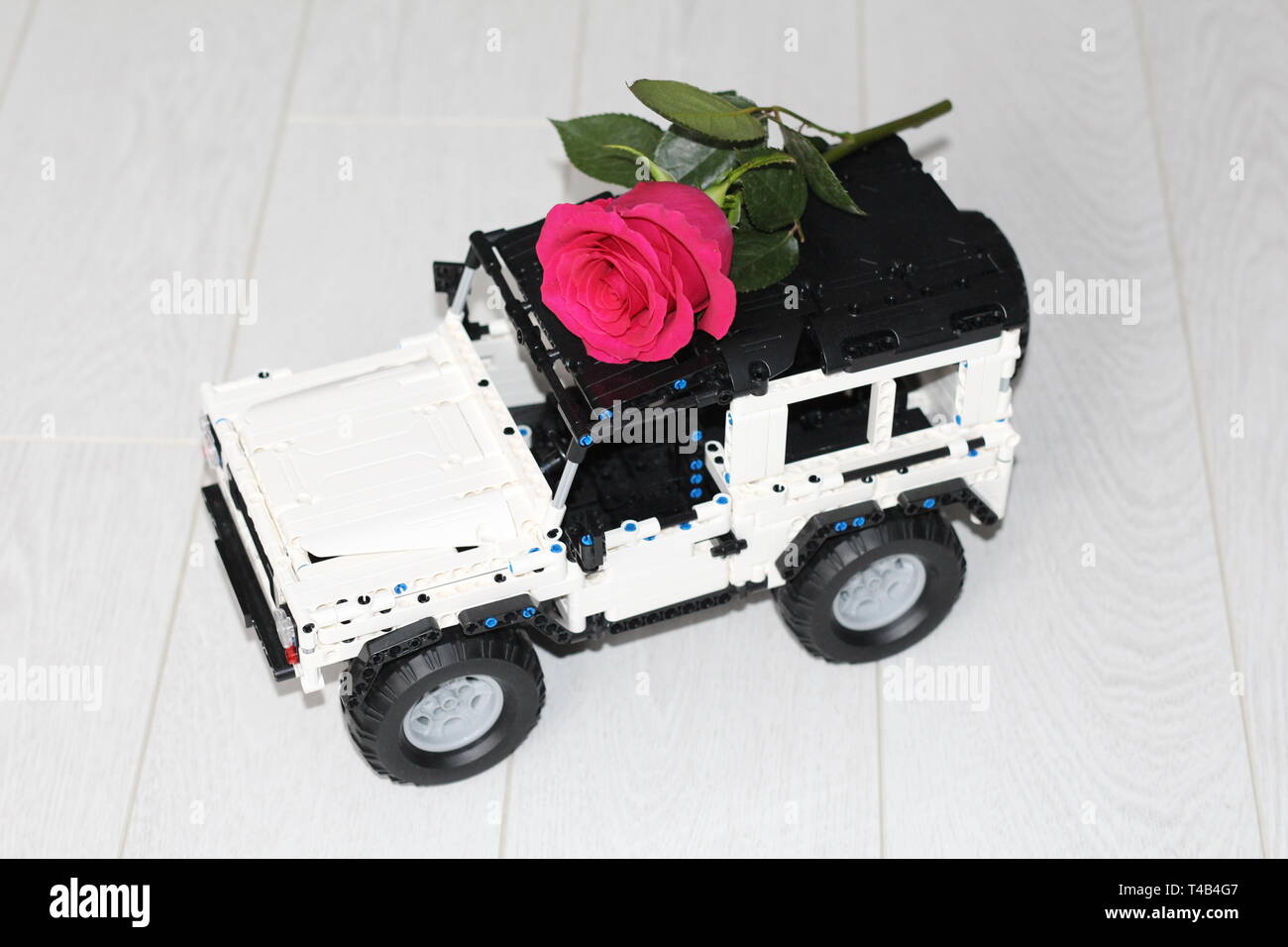 Das Spielzeug Auto SUV trägt eine rote Rose. Das Auto ist der Designer gemacht, es ist schwarz und weiß. Blume Lieferung. Stockfoto