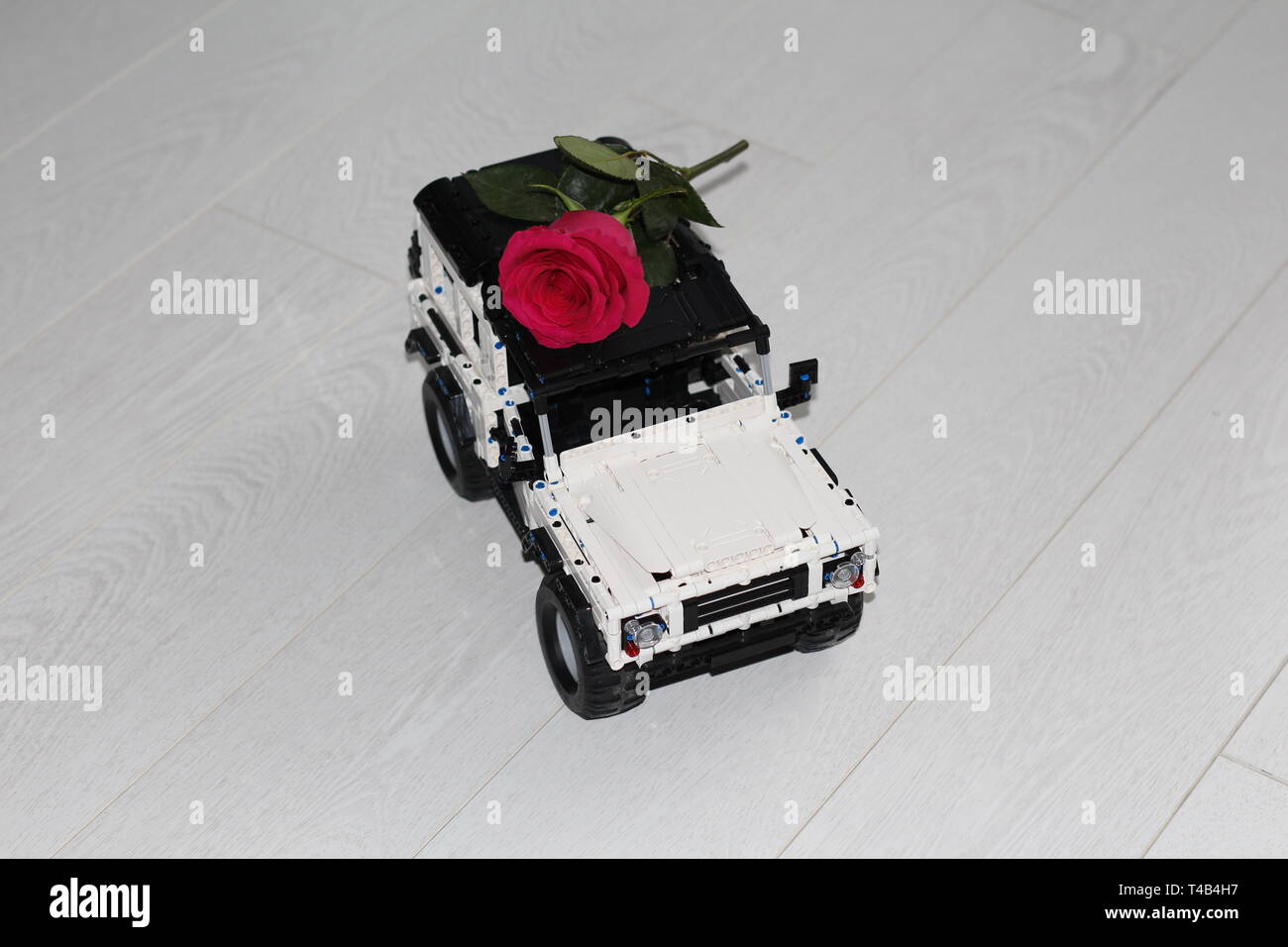 Das Spielzeug Auto SUV trägt eine rote Rose. Das Auto ist der Designer gemacht, es ist schwarz und weiß. Blume Lieferung. Stockfoto