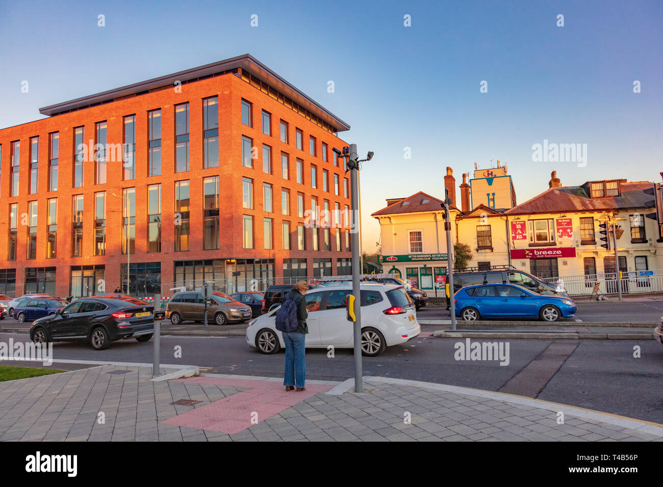 Eine Frau wartet eine vielbefahrene Straße inmitten der neuen Entwicklungen in Ashford Stadtzentrum in Kent, Großbritannien zu überqueren Stockfoto