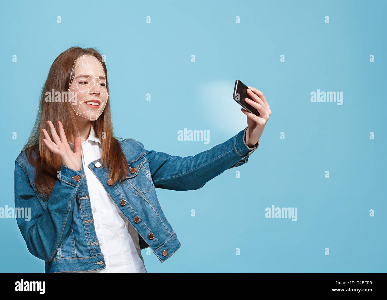 Etwas Neues auszuprobieren. Ein Mädchen mit einem Smartphone in Jeans Anzug stehen auf blauem Hintergrund. Die Technologie der Gesichtserkennung auf vieleckigen Netz. Konzept der Cyber Security, Business, Arbeit, Bildung. Stockfoto