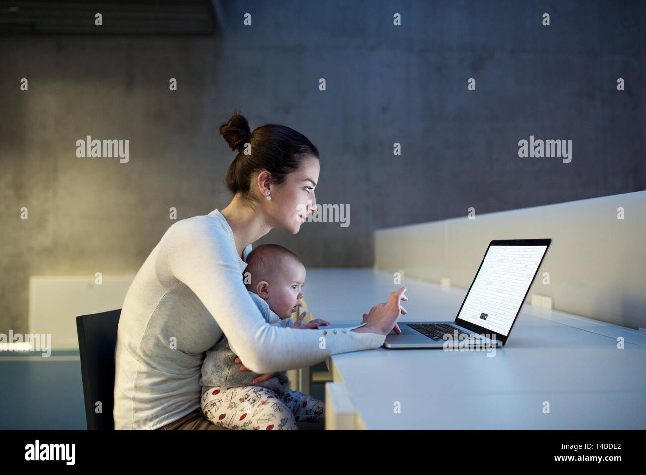 Junge Studenten mit einem Babysitter auf Schreibtisch im Zimmer in einer Bibliothek oder einem Büro, mit Laptop. Stockfoto