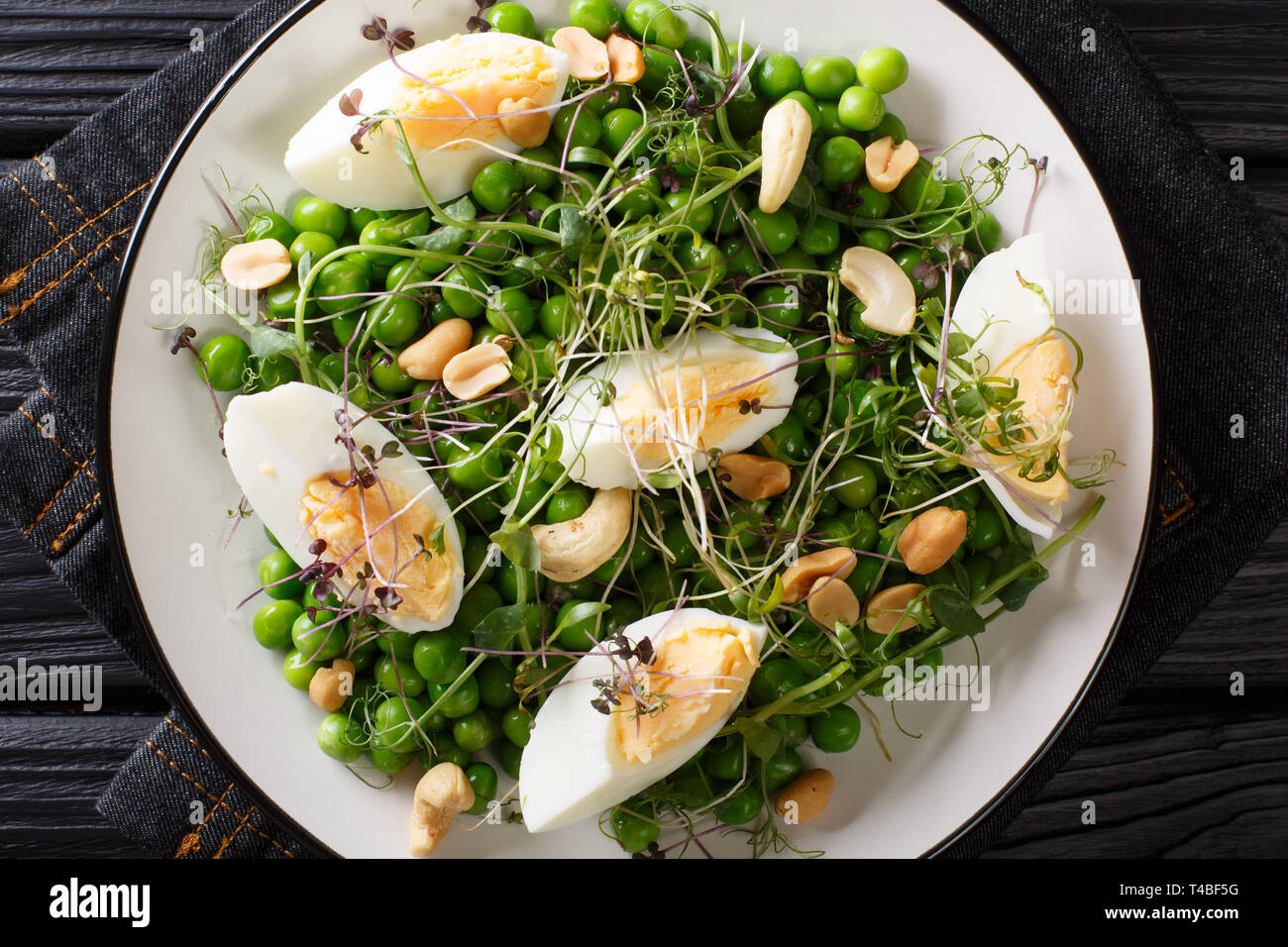 Organische vitamin Salat von grünen Erbsen, micro Grüns, Nüsse und Eier close-up auf einem Teller auf den Tisch. Horizontal oben Ansicht von oben Stockfoto