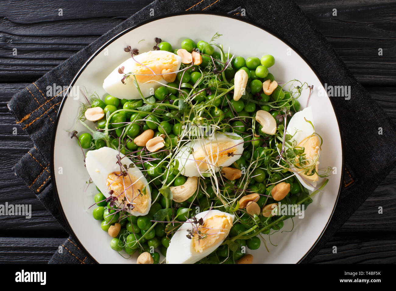 Leckeren, gesunden Salat von grünen Erbsen, micro Grüns, Nüsse und Eier close-up auf einem Schild auf dem Tisch gekocht. horizontal oben Ansicht von oben Stockfoto