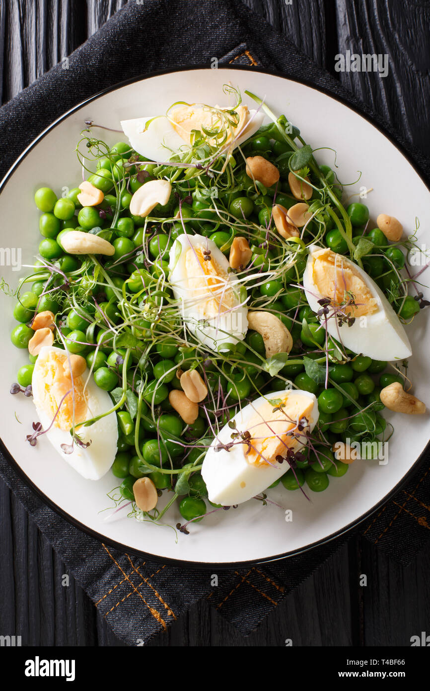 Organische vitamin Salat von grünen Erbsen, micro Grüns, Nüsse und Eier close-up auf einem Teller auf den Tisch. Vertikal oben Ansicht von oben Stockfoto